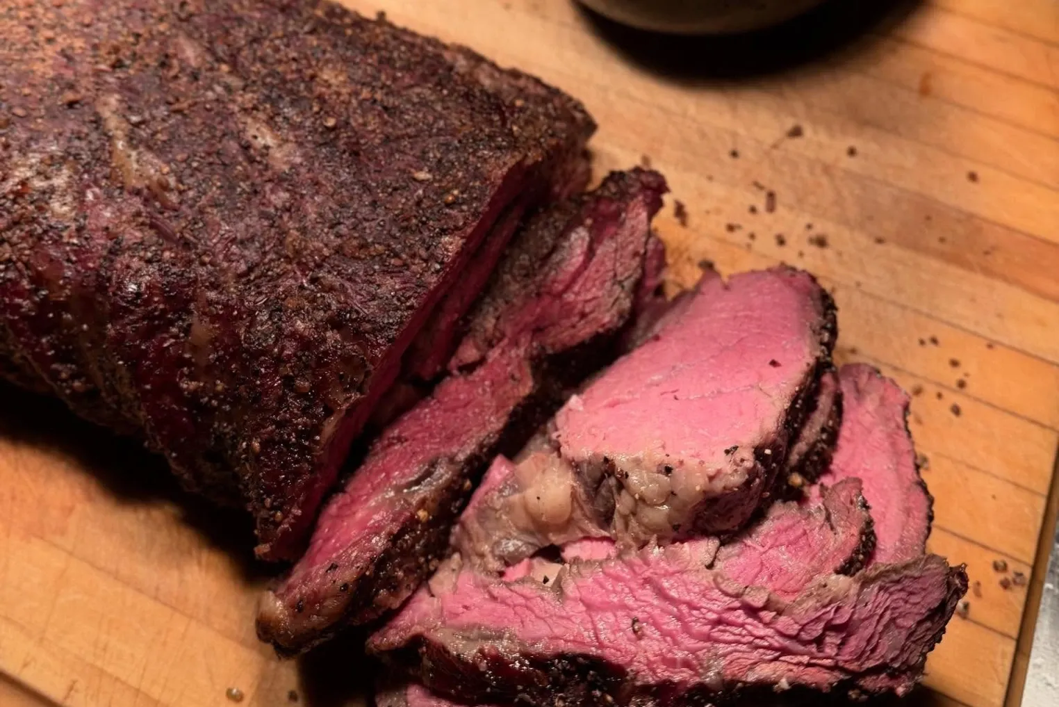 Sliced smoked beef with a rosy center on a carving board