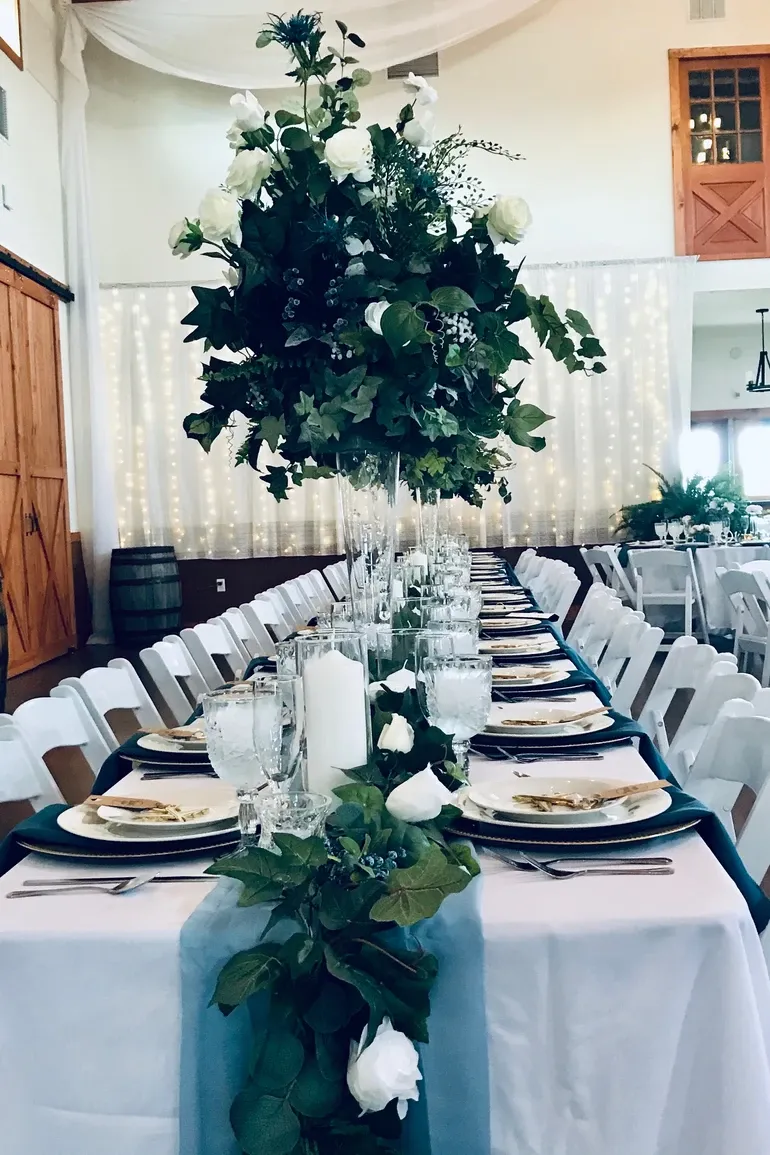 Long royal table with tall greenery centerpieces under curtain lights